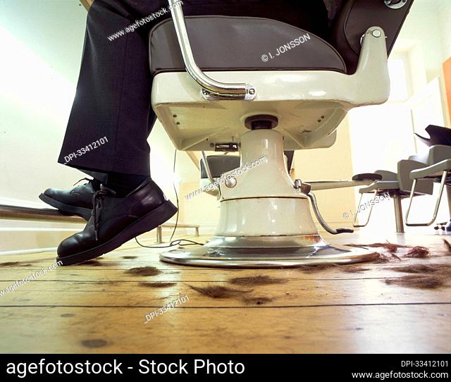 Legs and feet of a person sitting in a hairdresser's chair getting a haircut with hair clippings on the floor; Germany