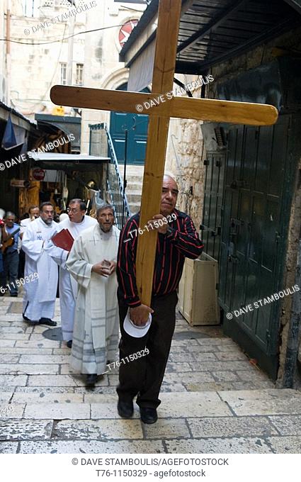 a pilgrim carries the cross following Jesus' steps on the Via Dolorosa in Jerusalem