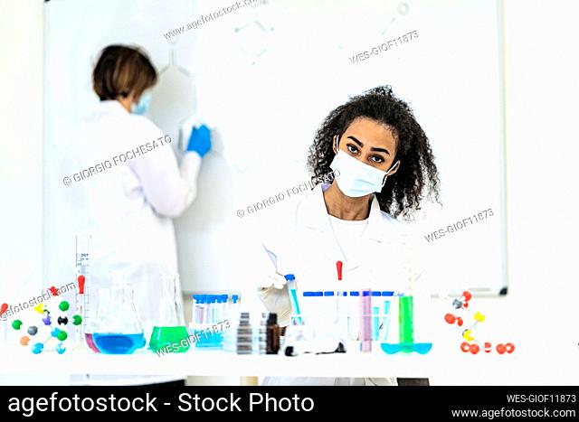 Female researcher working while coworker drawing on whiteboard in laboratory