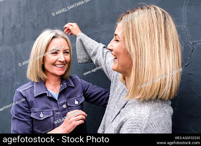 Senior woman looking at daughter laughing in front of wall