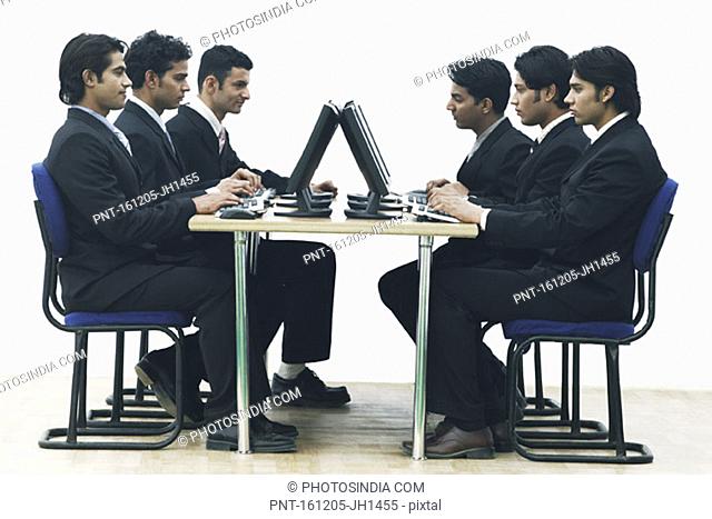 Side profile of a group of businessmen working on computers in an office