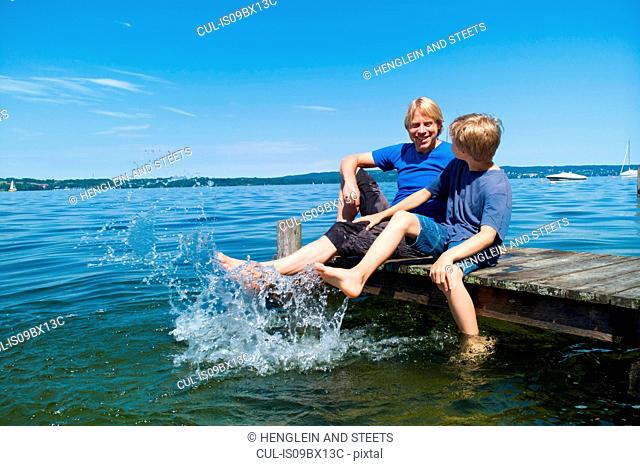 Father and son cooling feet in water, Lake Starnberg, Bavaria, Germany