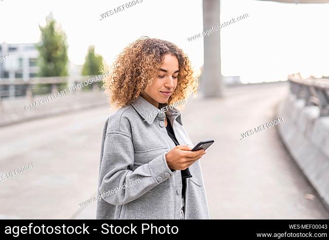 Beautiful young Afro woman using smart phone while standing on bridge in city