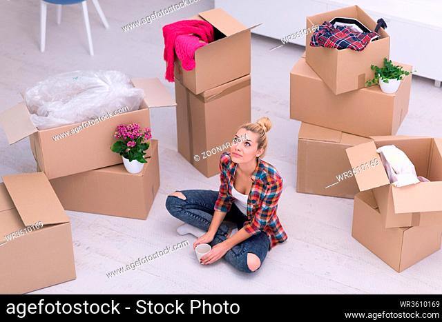 people, moving new place and repair concept  happy beautiful young woman with many cardboard boxes sitting on floor with Cup at home