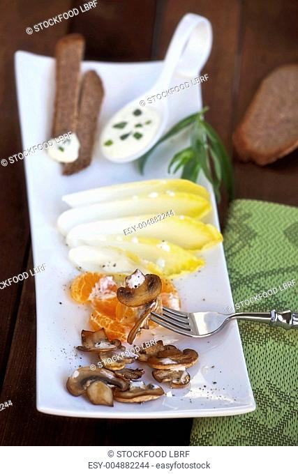 A salad platter of chicory, mandarins, mushrooms and bread