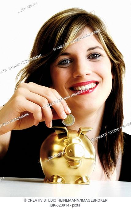 Young woman inserting money into a golden piggy bank
