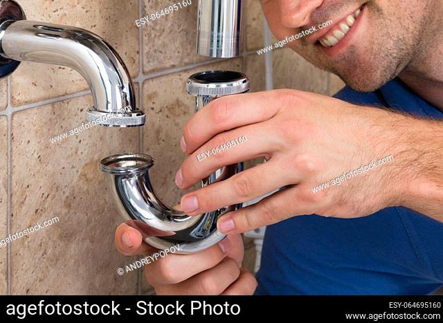 Young Male Plumber Fitting Sink Pipe In Bathroom