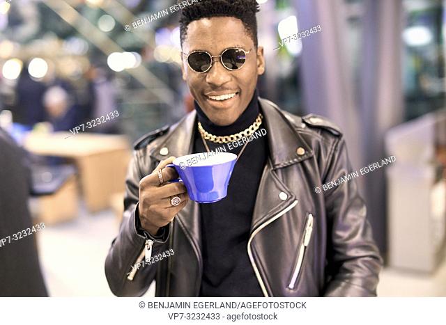 young fancy man holding coffee cup and smiling happily, African descent, in Munich, Germany