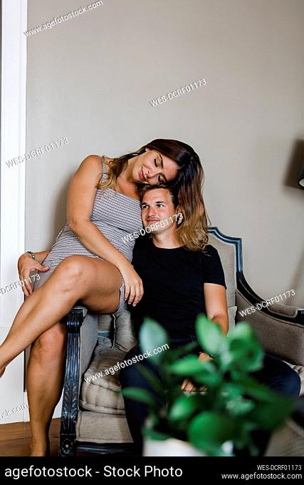 Smiling woman with eyes closed sitting by boyfriend on armchair at home