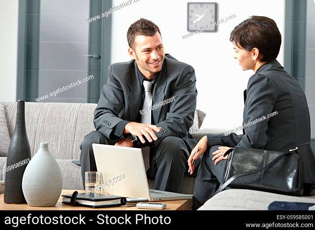 Young business people having meeting at office sitting on sofa talking