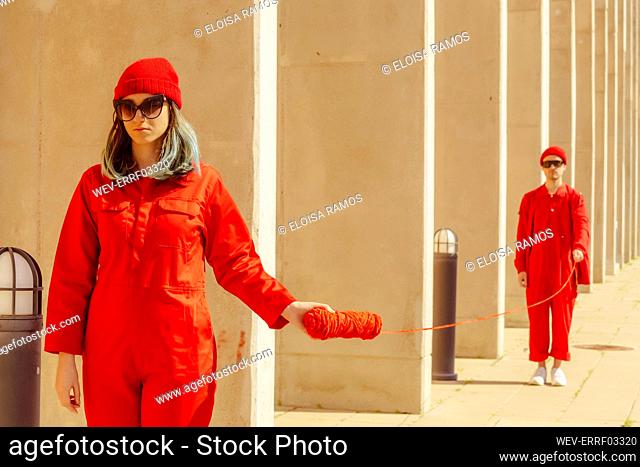 Young couple wearing red overalls and hats standing in a row connected with red string