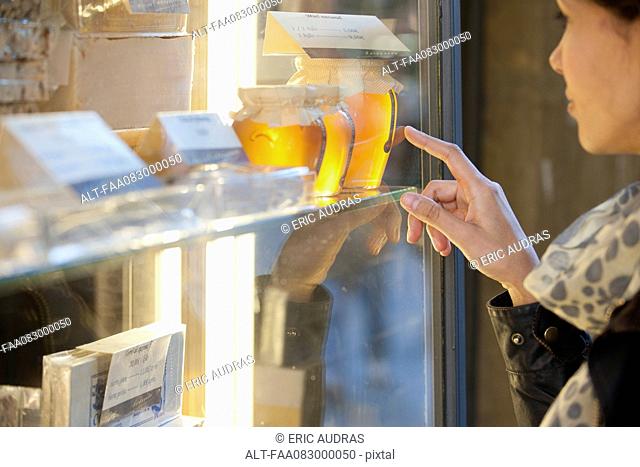 Woman looking at jars of honey in shop window