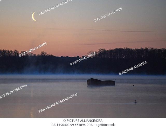 01 April 2019, Brandenburg, Groß Schauen: The crescent of the waning moon shines shortly before sunrise over the nature reserve Groß Schauener Seenkette