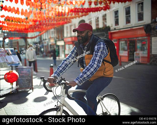 Man riding bike on sunny city street, Chinatown, London, UK