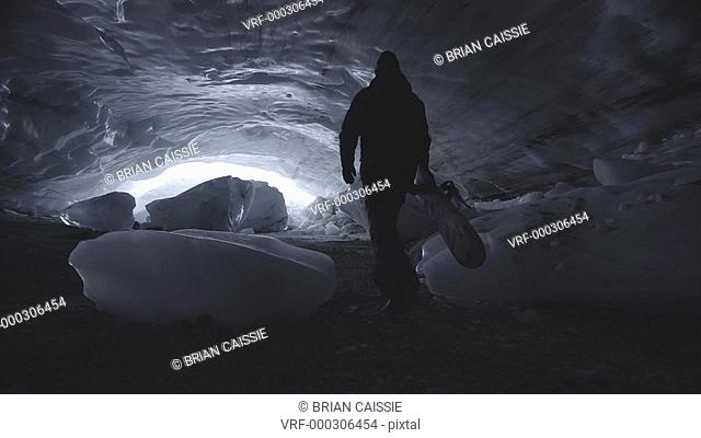 Tracking shot of man with snowboard walking in glacier cave, Whistler, British Columbia, Canada