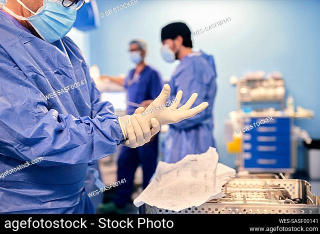 Mature doctor wearing protective glove while standing at operation room