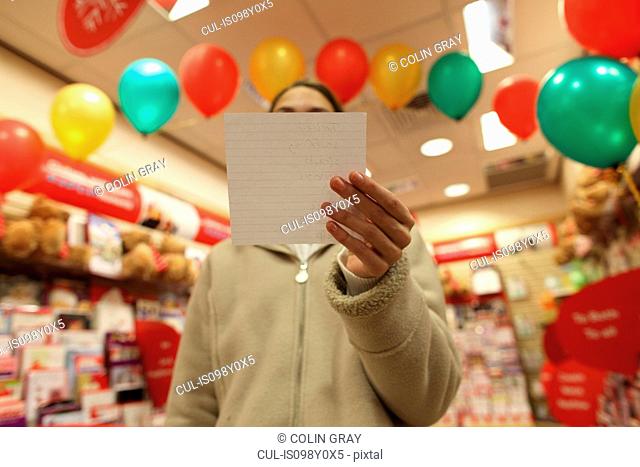 Teenage girl in shop with shopping list covering face