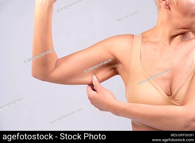 Woman pulling muscle skin while standing against gray background