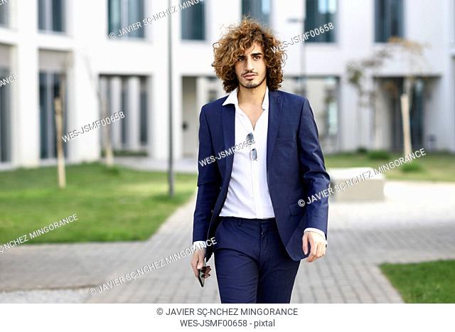 Portrait of young fashionable businessman with curly hair wearing blue suit