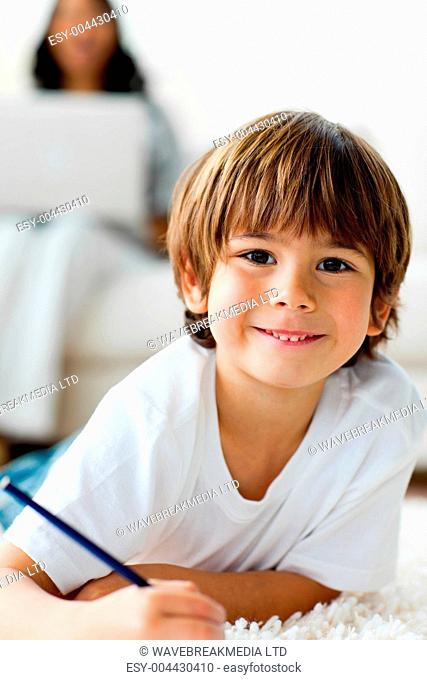 Smiling little boy drawing lying on the floor
