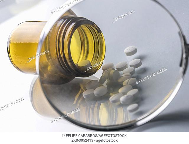Pill bottle seen through a magnifying glass isolated in white background, conceptual image