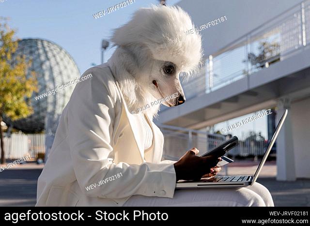 Woman in dog mask using mobile phone and credit card for online shopping