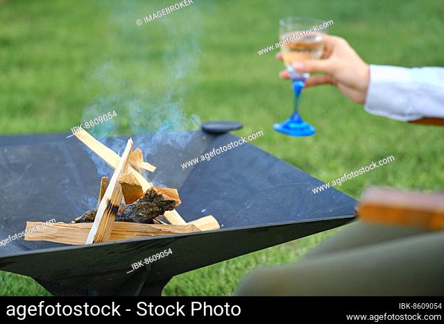 Firewood in the grill outdoor and defocused hand with a glass of lemonade on background