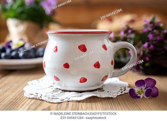 Polka dot mug on a table, with purple dead-nettles, pansies and blueberries in the background