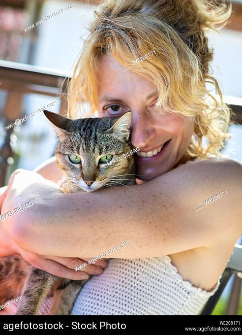 portrait of a young mature caucasian blonde woman smiling with her cat at home on the porch sitting in a rocking chair. Lifestyle concept