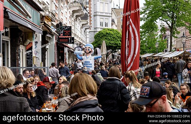 30 April 2022, Hamburg: The sidewalk cafes in Hamburg's Schanzenviertel district are filled with visitors, while a sign for a Corona test center also located...