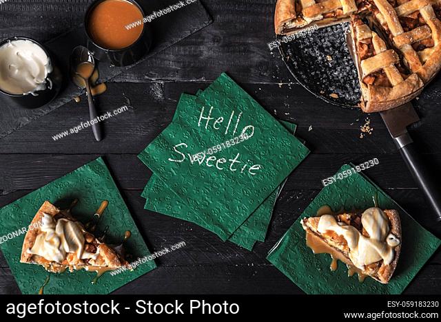 Apple pie and slices with cream and caramel topping, and a napkin with the words hello sweetie, on a table. Sweetie pie context. Traditional dessert