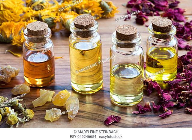 Bottles of essential oil with dried rose petals, chamomile, calendula and frankincense on a wooden table