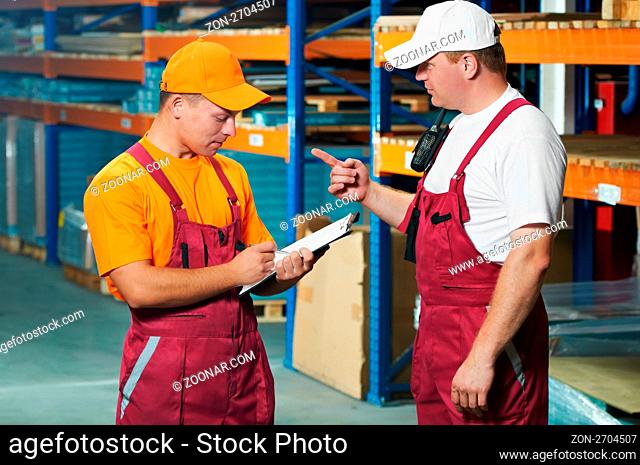 two young workers man in uniform in front of warehouse rack arrangement stillages