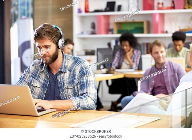 Businessman Wearing Headphones Working On Laptop In Office