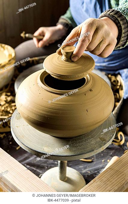Ceramics workshop, hand holding lid on opening of can over pottery wheel, Pittenhart, Upper Bavaria, Germany