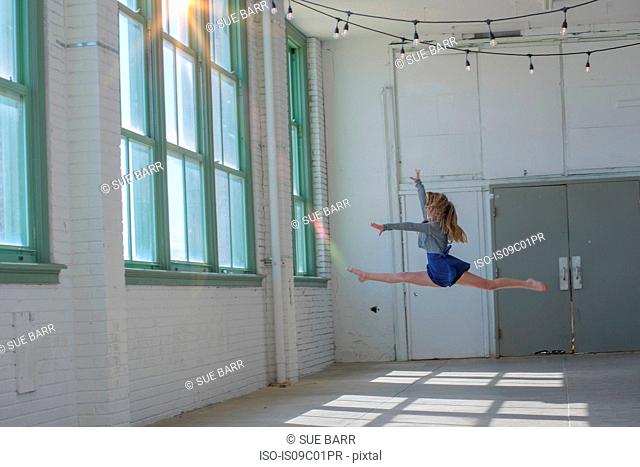 Teenage girl with long brown hair leaping mid air in dance studio