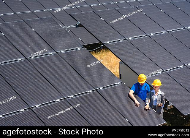 Two people standing amid solar cells in a power plant inspecting the modules
