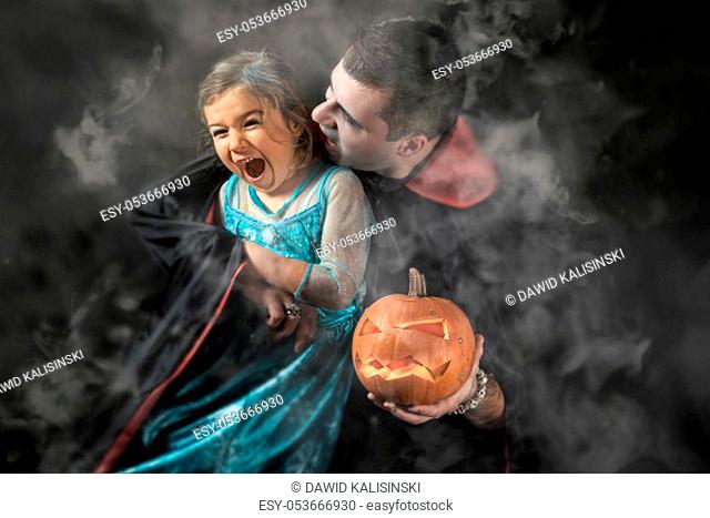Halloween portrait vampire attacking young princess father and daughter play adult Caucasian white man holding orange pumpkin smoke or fog background