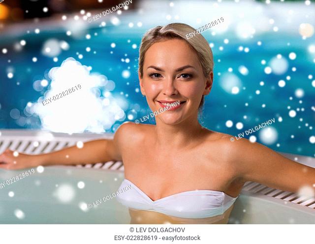 people, beauty, spa, healthy lifestyle and relaxation concept - beautiful young woman wearing bikini swimsuit sitting in jacuzzi at poolside with snow effect