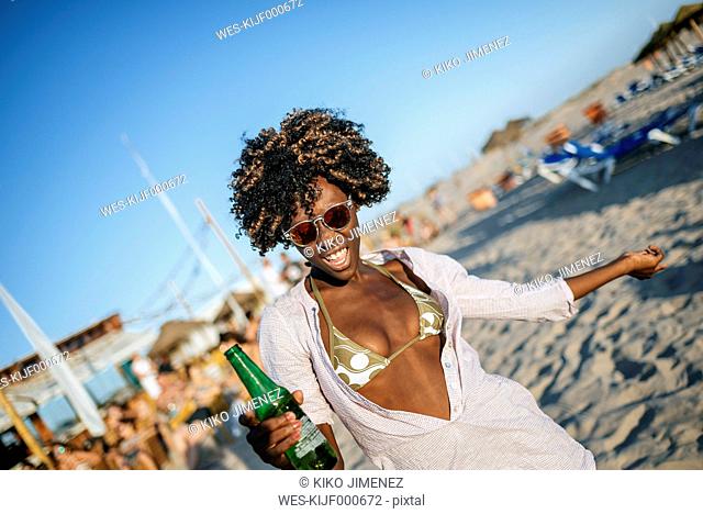 Young woman dancing on the beach with a beer in her hand