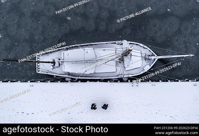 06 December 2023, Mecklenburg-Western Pomerania, Kirchdorf (poel): Two holidaymakers walk past a sailing ship covered in snow and frozen in thin ice in the...