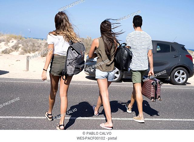Friends crossing road, carrying bags, going to the beach