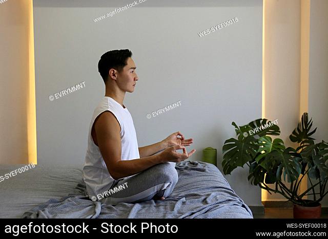 Young man practicing yoga sitting on bed at home