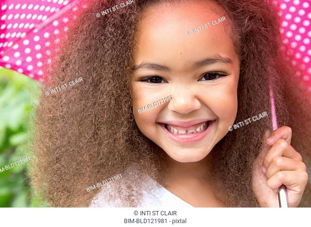 Mixed race girl smiling under umbrella