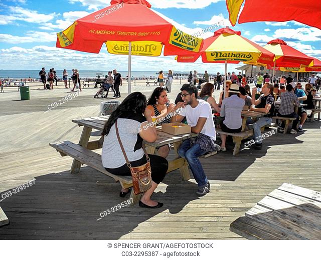 Multiracial locals enjoy a sunny day on the boardwalk at Coney Island, New York City. Note umbrellas from the famous Nathan's restaurant