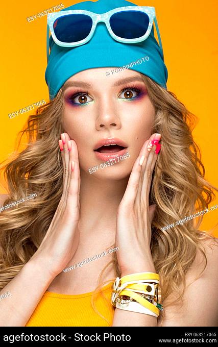 Bright cheerful girl in a sports hat, colorful make-up, curls and pink manicure. Beauty face. Photo taken in the studio