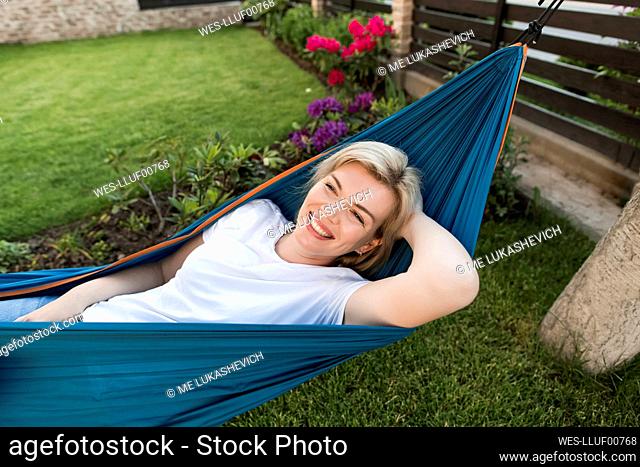 Happy mature woman lying on hammock in garden