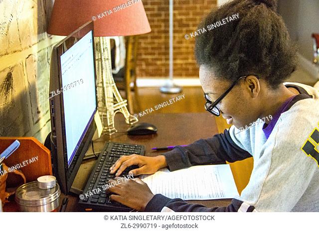 African American teenager, with glasses, 15 years old, working on homework at her home in front of the desktop computer