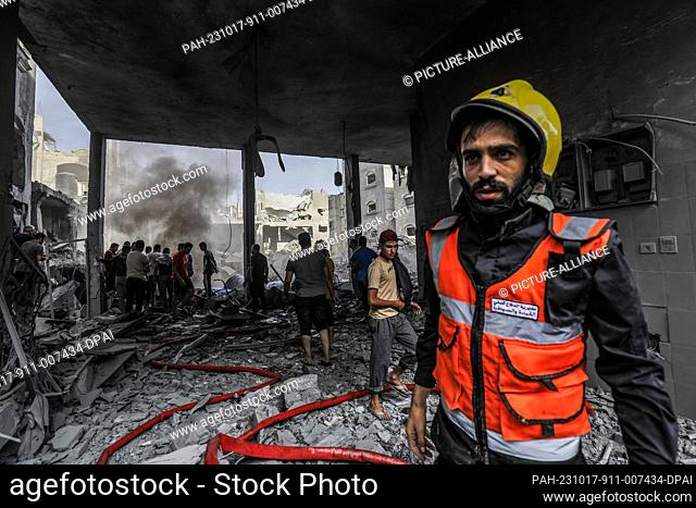 17 October 2023, Palestinian Territories, Rafah: A member of the Palestinian Civil Defense recovers bodies and injured people from under the rubble after an...