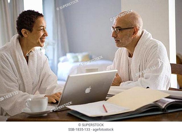 Mature woman working on a laptop and looking at a mature man sitting beside her